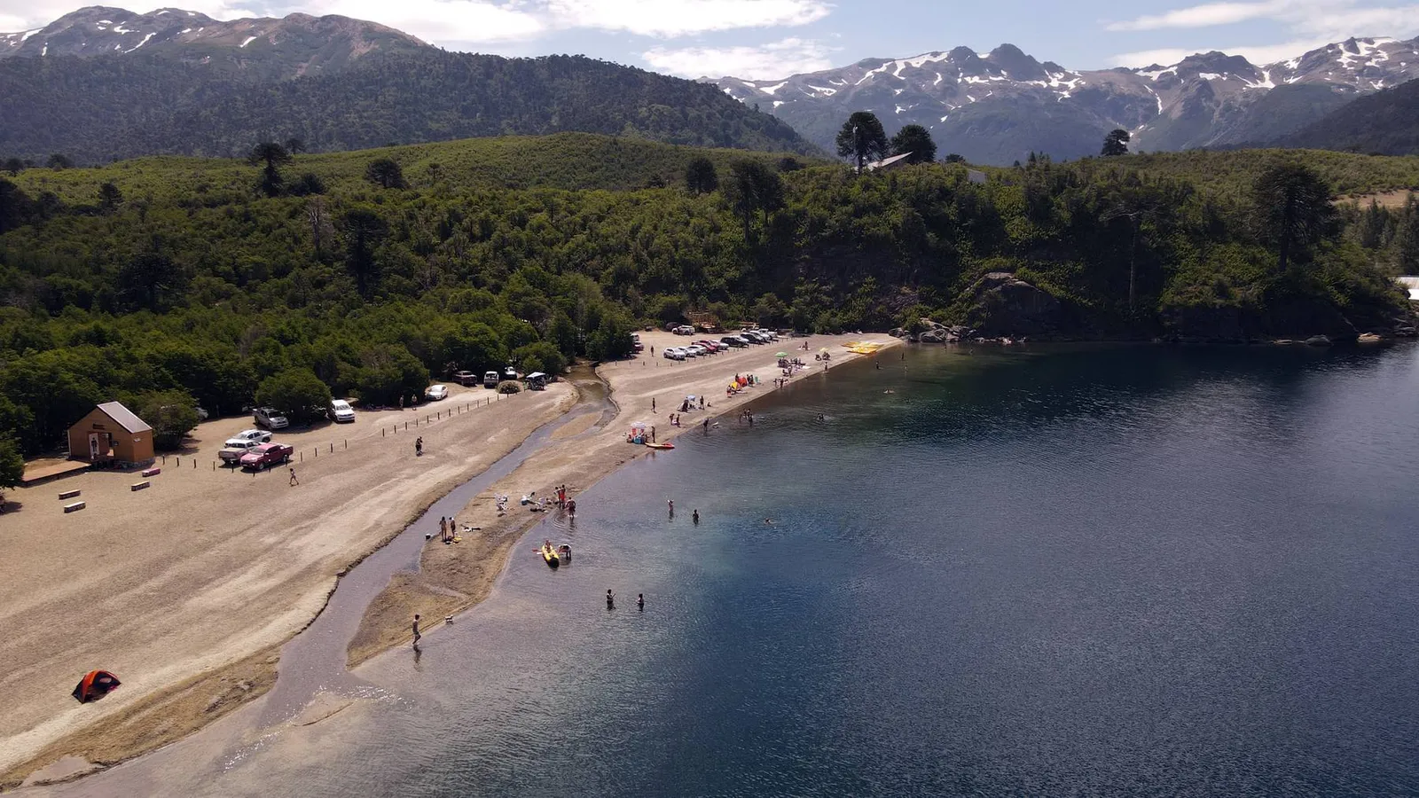 Vista aérea de la playa y el lago en Villa Pehuenia, con la cordillera nevada de fondo